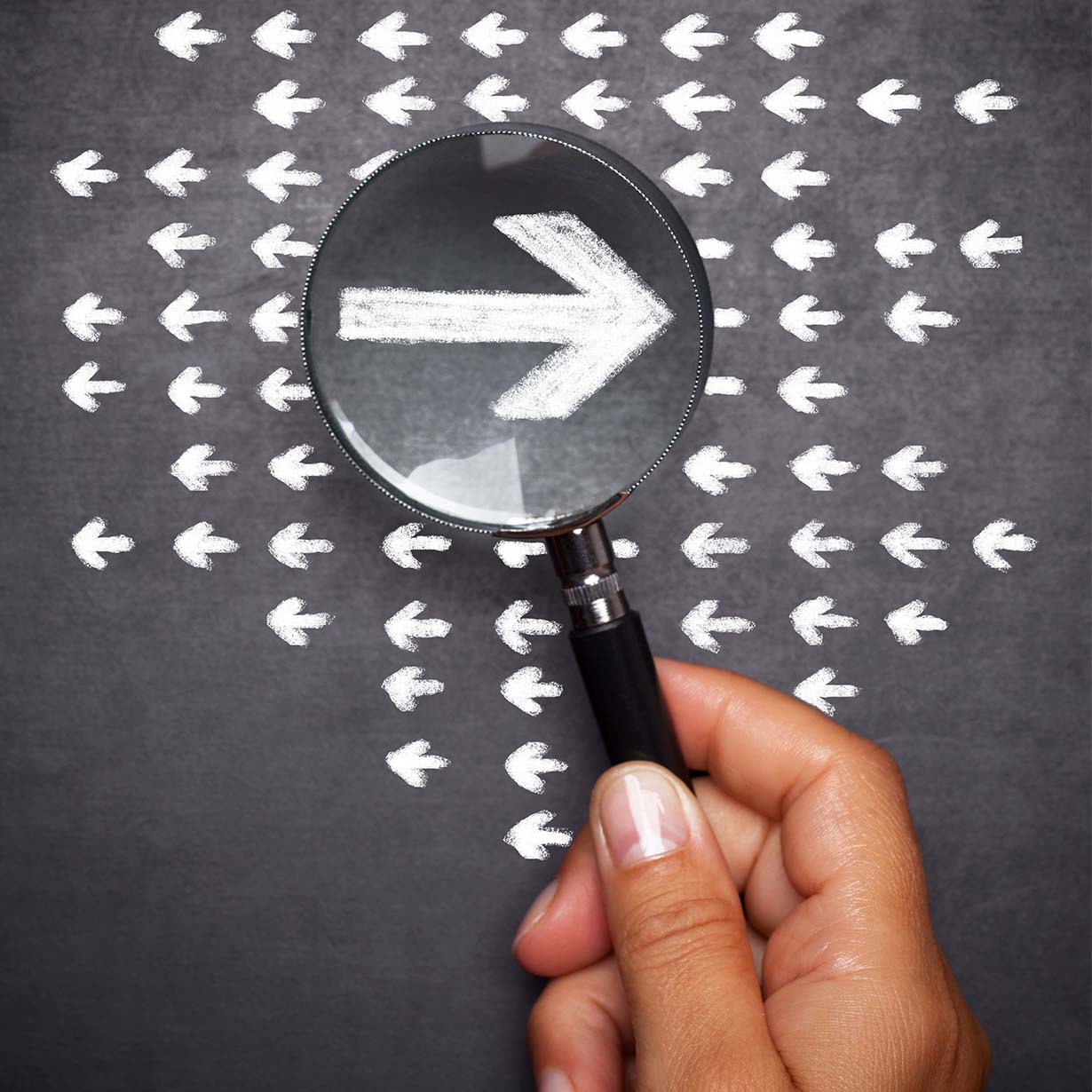 Multiple drawn white arrows on a dark background, hand holding a magnifying glass over one arrow, which is going the opposite direction