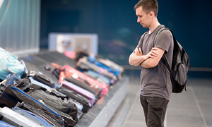 Potnik z zaskrbljenim izrazom stoji ob tekočem traku za prtljago na letališču.