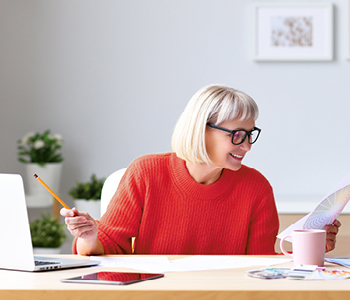 Ženska sedi v svoji domači pisarni in samozavestno pregleduje svoj mesečni proračun, saj ve, kaj je varčevanje in za kaj varčuje.
