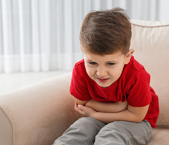 Deček na sliki se drži za trebuh in pači zaradi bolečin. Kako odpraviti bolečine v trebuhu pri otrocih je pogosto vprašanje staršev majhnih otrok.