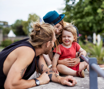 Mlada družina uživa v parku - oba starša pozorno opazujeta razigranega otroka, ker ga želita zaščititi