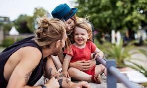Mlada družina uživa v parku - oba starša pozorno opazujeta razigranega otroka, ker ga želita zaščititi