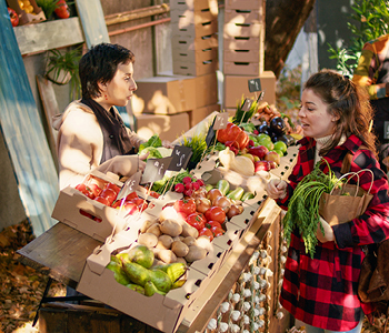 Mlada ženska na stojnici pri lokalnem pridelovalcu kupuje lokalno pridelano sadje in zelenjavo - brez plastične embalaže.
