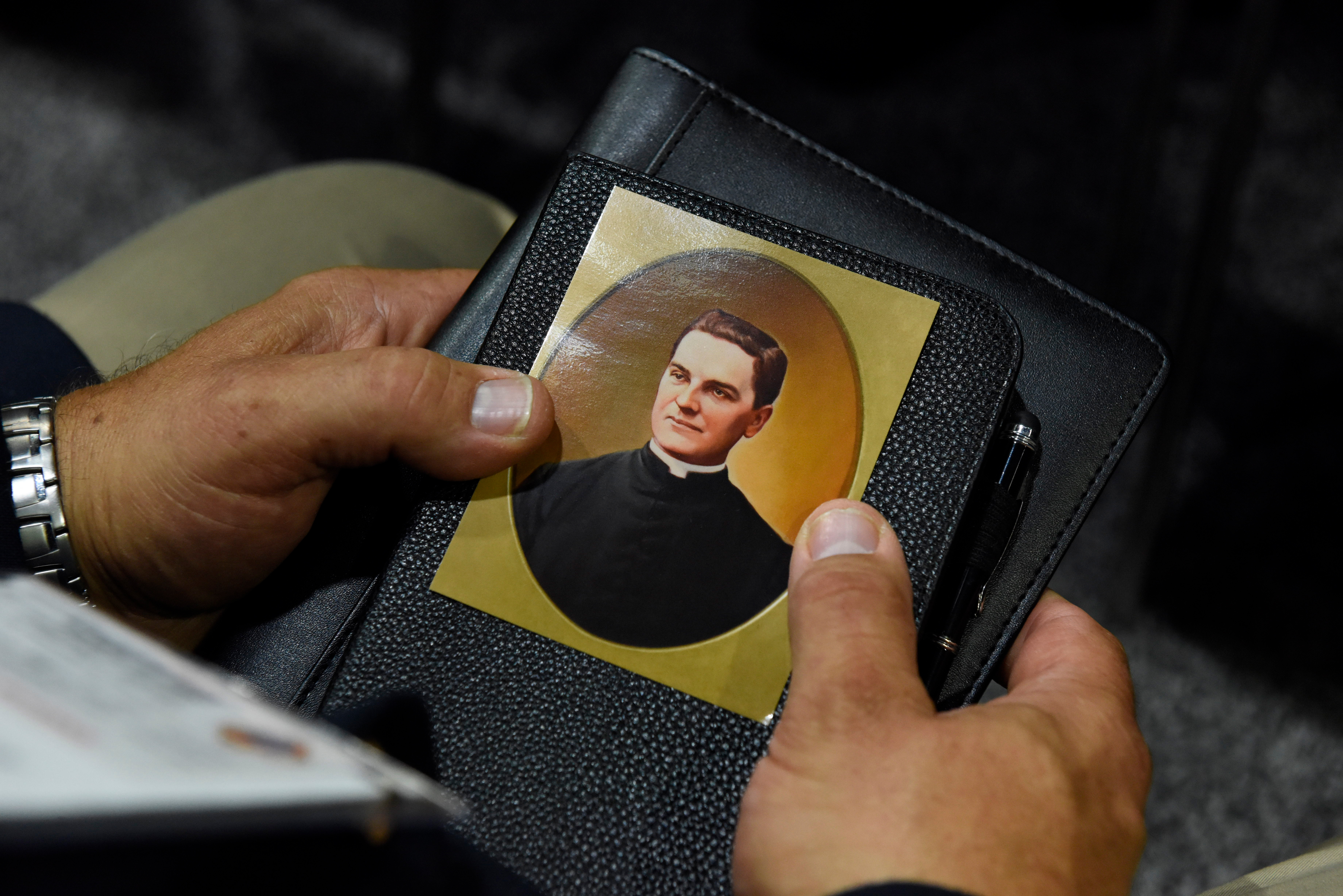 A devotee praying to Father McGivney holding his prayer card.