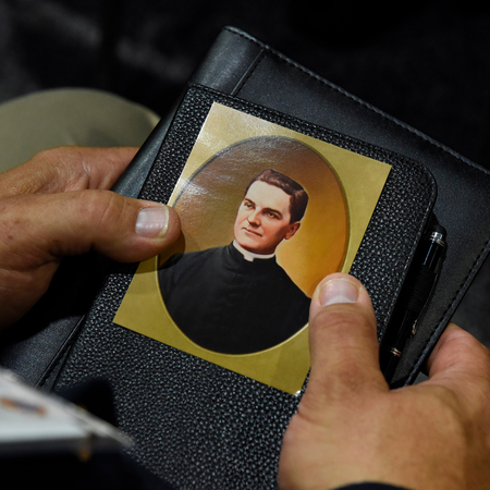 A devotee praying to Father McGivney holding his prayer card.