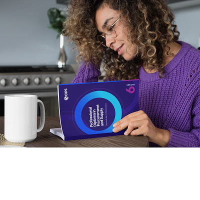A woman with curly hair wearing a purple sweater and glasses is sitting at a counter, looking down at a booklet titled 
