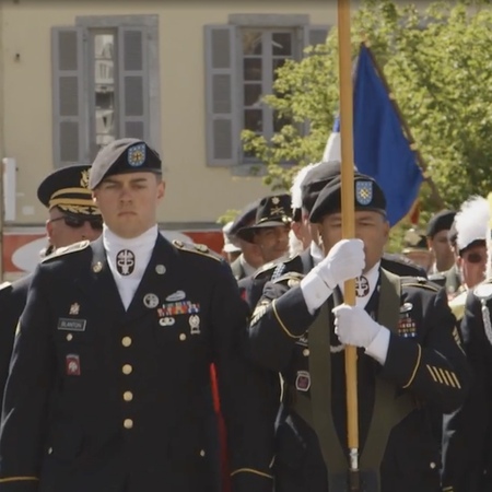 Military members march in a procession while holding a flag pole