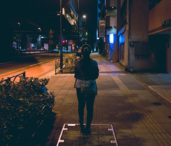 Ženska na ulici ponoči je v temnih oblačilih celo pod uličnimi svetilkami slabo vidna