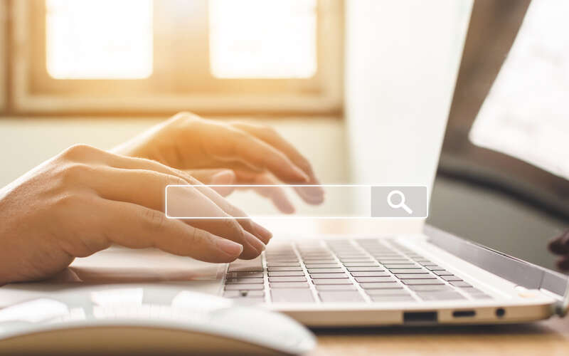 Hands of man typing on laptop keyboard, a search box is superimposed over the image.