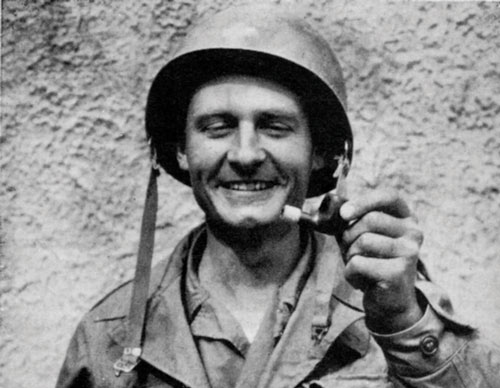 Chaplain Emil Kapaun smiles as he holds up a pipe broken by a sniper&rsquo;s bullet.