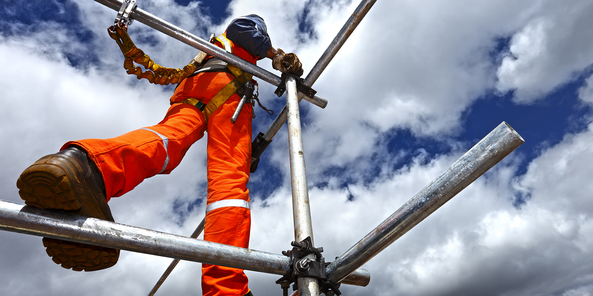 Construction worker in hi-vis vest walking on a metal structure, working on building construction
