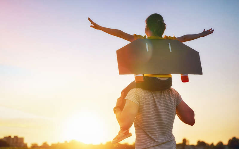 A child, with wings made of cardboard, is being carried by a man.