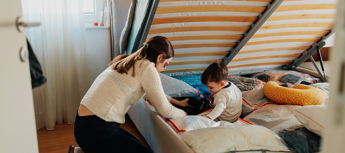 A mother and son storing items under a bed mattress.