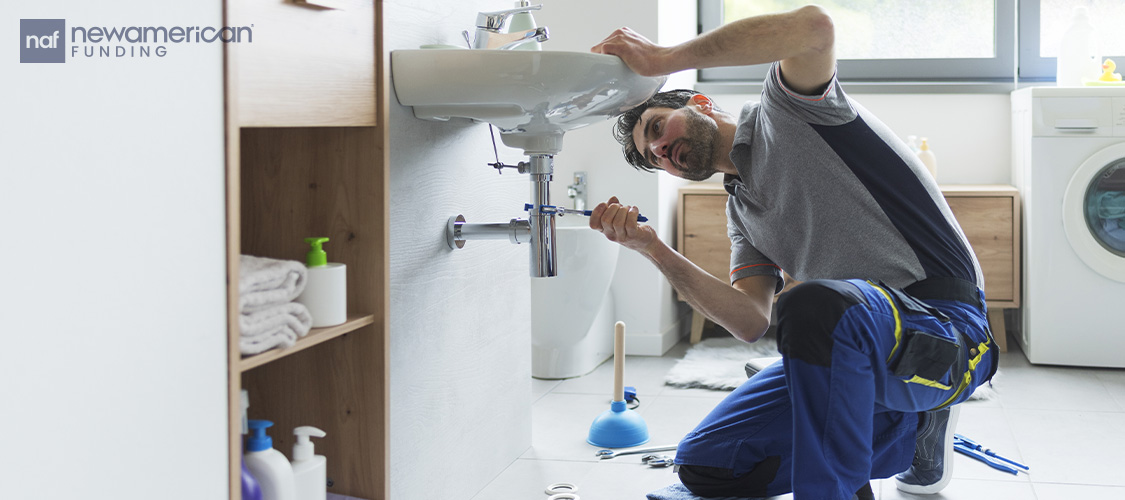 A man fixing the pipes under a sink.
