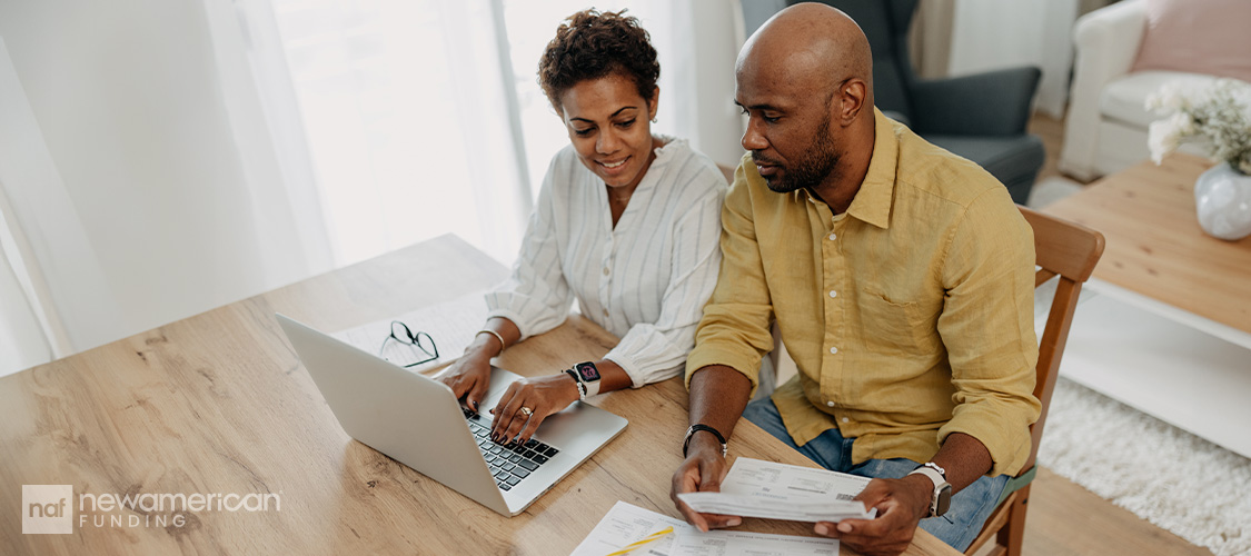 A smiling couple looking at paperwork and a laptop.