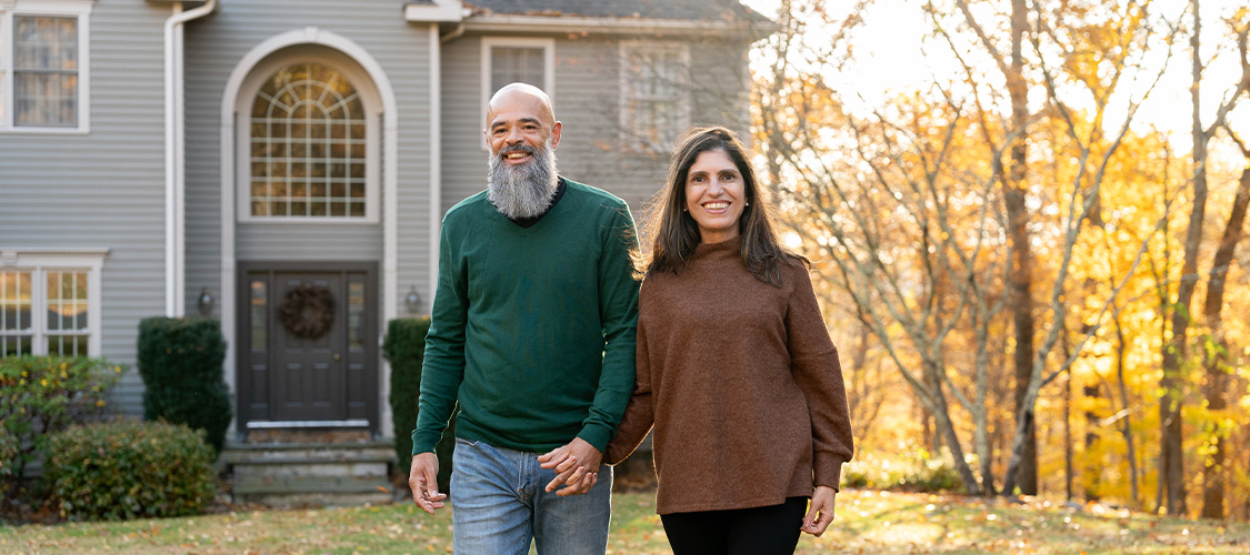 And older couple walking outside of a home in the fall.