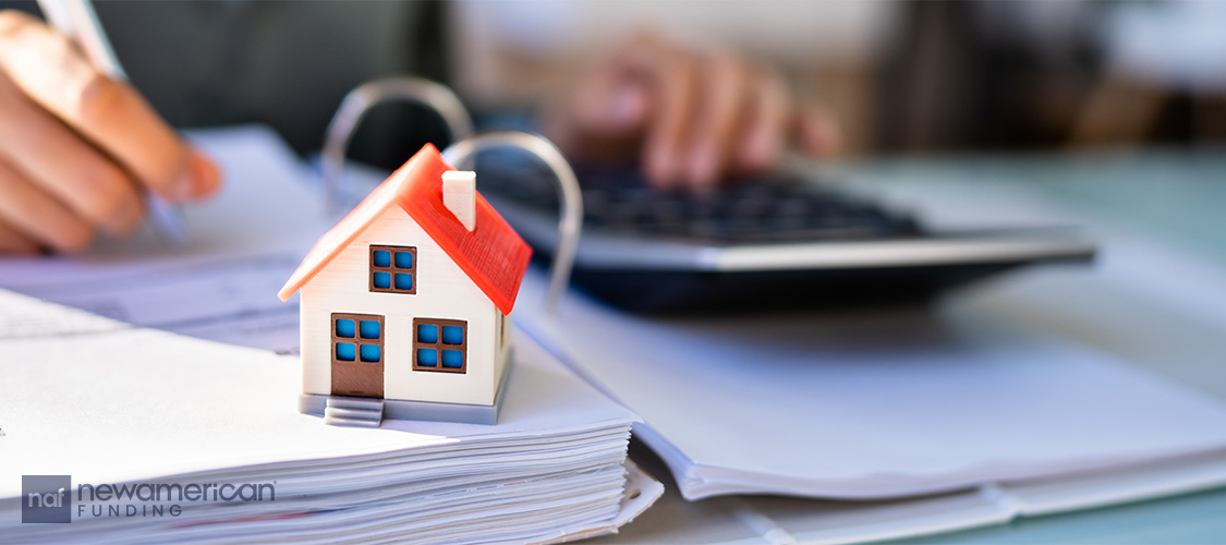 A person using a calculator with a small model of a house