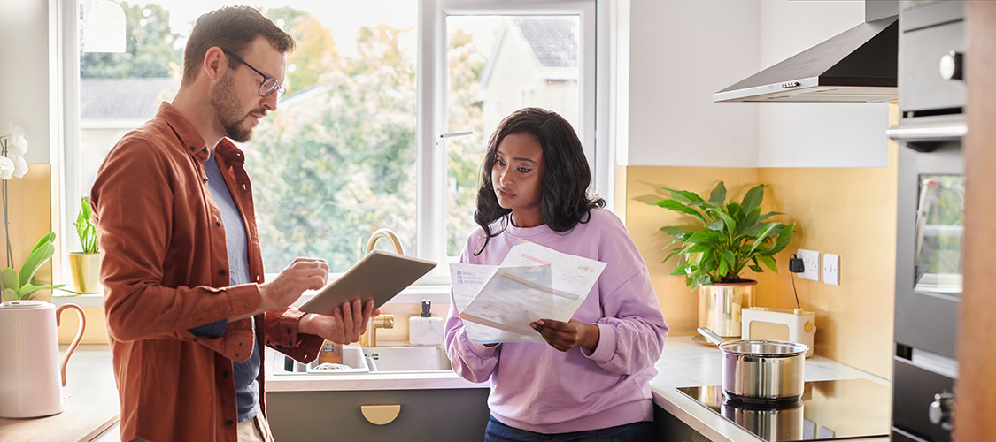 A couple looking at paperwork as they stand in a kitchen.