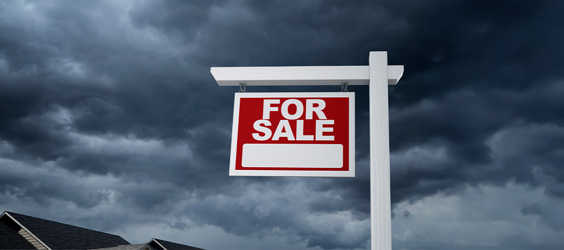 A for sale sign with storm clouds behind it