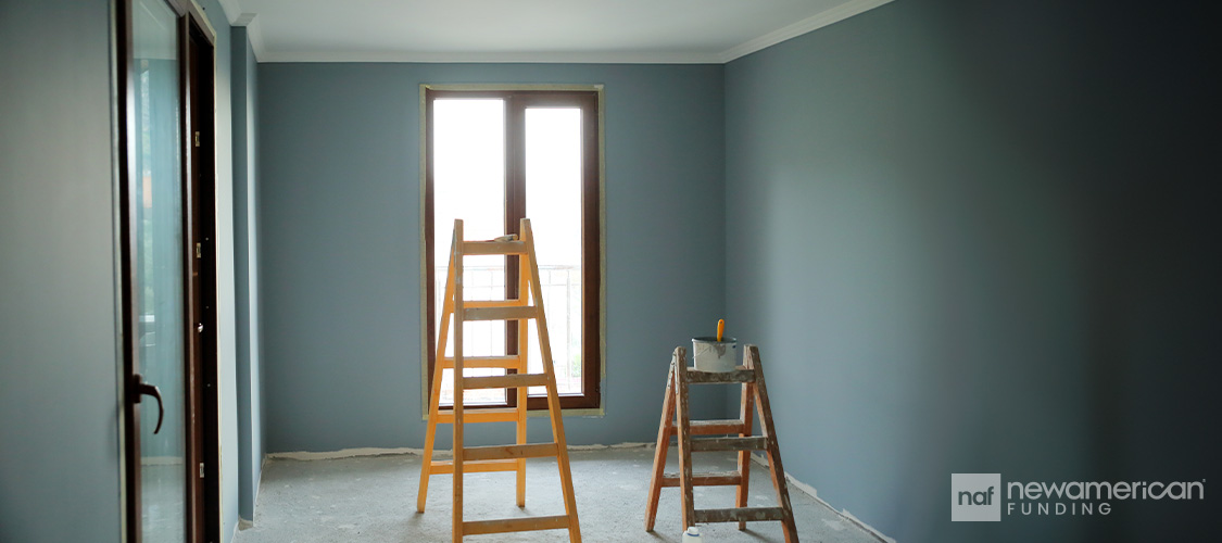 Two ladders in the center of an empty, newly painted green room.