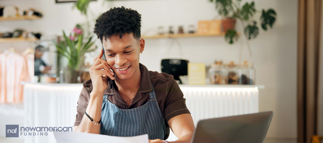A person in an apron on the phone looking at paperwork.
