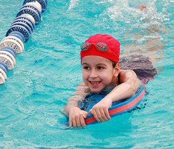 Deklica, ki obiskuje plavalni tečaj za otroke, v bazenu čofota z učnim pripomočkom