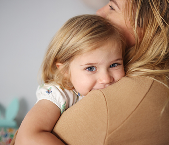 Deklica se skriva v maminem objemu in nagajico smehlja - podkožna bulica je ne skrbi, saj so ju zdravniki pomirili.