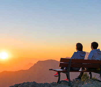 Pokojninsko zavarovanje sklenite, ko ste mladi - mlad par sedi na klopci v hribih in občudije sončni vzhod