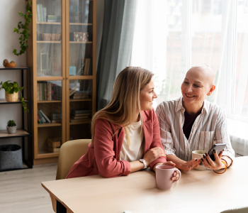 Dve ženski srednjih let v domači kuhinji v prijetnem vzdušju pijeta kavo. Ena je obrita in očitno preboleva raka, druga pa ji nudi oporo.