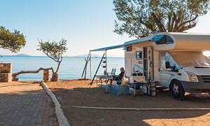 Avtodom z razprto tendo, parkiran na obali ob sončnem zahodu.
