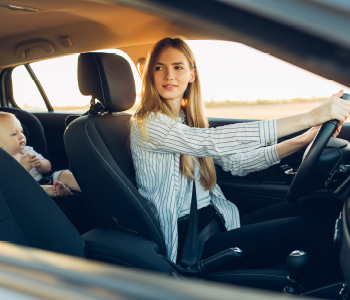 Mlada ženska za volanom avtomobila v poletnih mesecih uporablja klimo, da je njeni družini med vožnjo udobno.