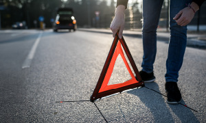 Voznik zaradi prometne nesreče postavlja varnostni trikotnik kot opozorilo drugim voznikom.