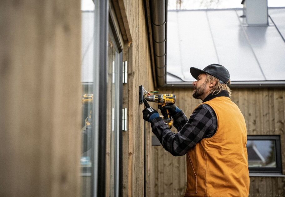 Man in safety gear installing electrical fixture on exterior wall of timber home