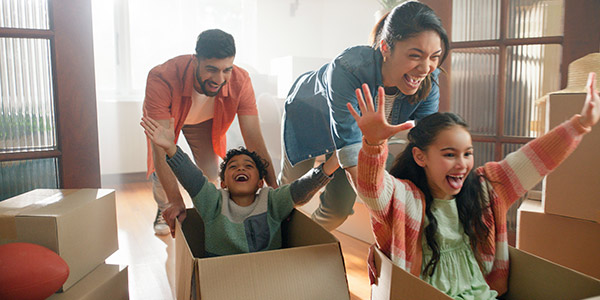 parents pushing their children in moving boxes in their new home