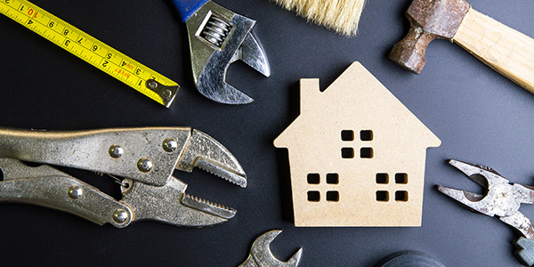 A model of a house sits on a table top surrounded by wrenches, pliers, and a tape measure