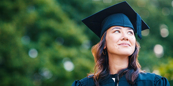 An Asian woman wearing a cap and gown smiles hopefully