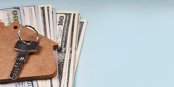 A stack of hundred dollar bills and a set of house keys sit on a table top