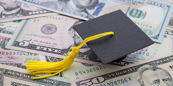 A graduation cap sits on top of a pile of cash