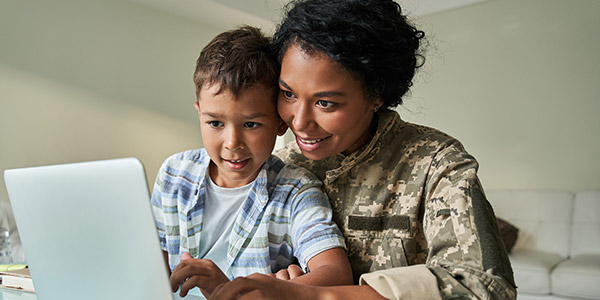 A Black woman wearing an American military uniform sits with a boy in her lap looking at a laptop