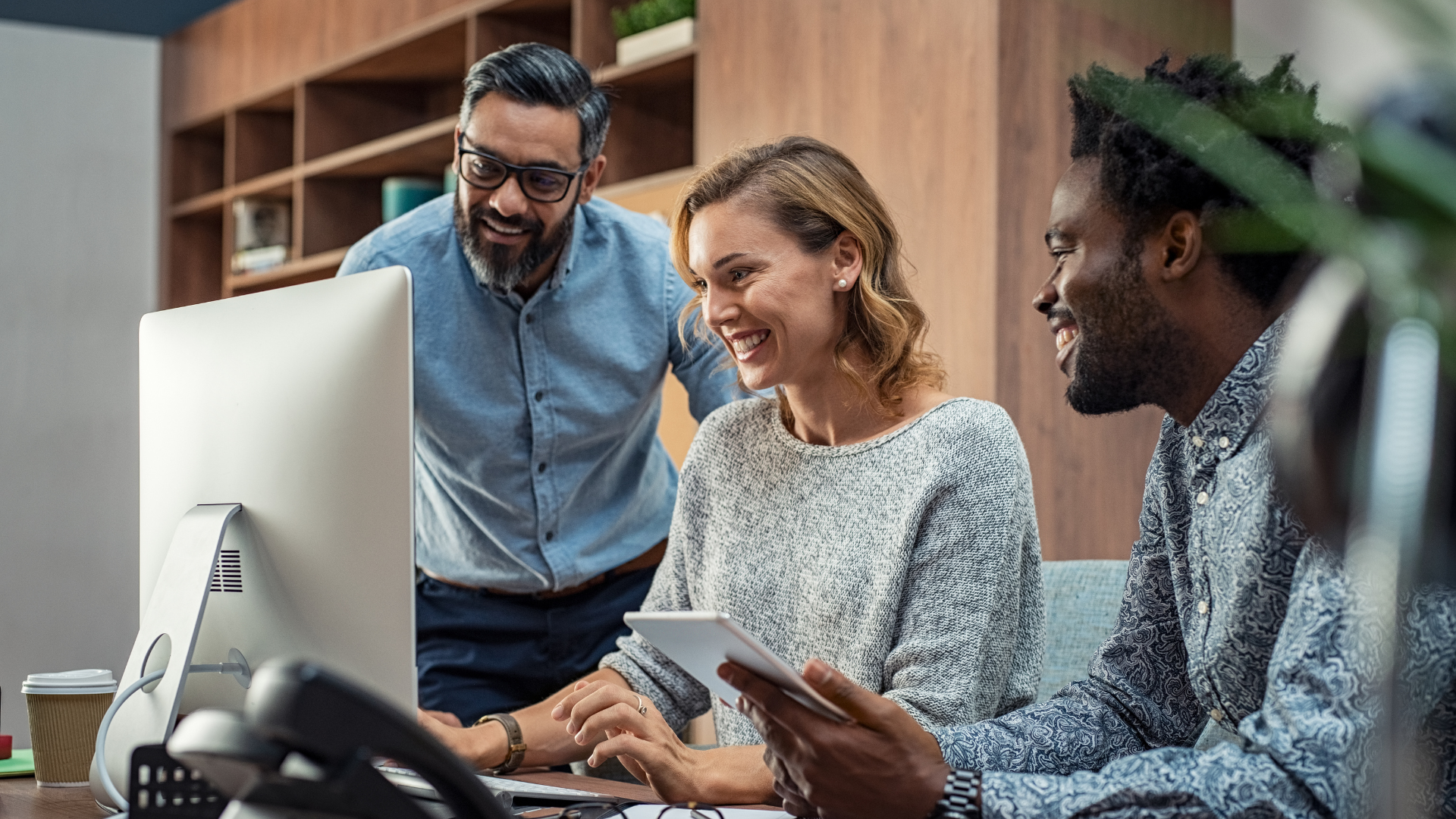 Three colleagues—two men and one woman—smiling and collaborating around a computer screen in a modern office. Overlaid text at the bottom reads: "Using data to drive ethical supply chains and uphold human rights."
