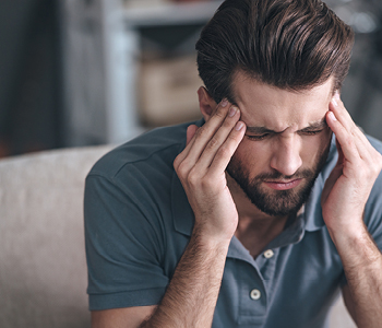 Mlad moški se drži za glavo zaradi bolečin in se sprašuje, če ni zanjo morda kriv tumor v glavi.