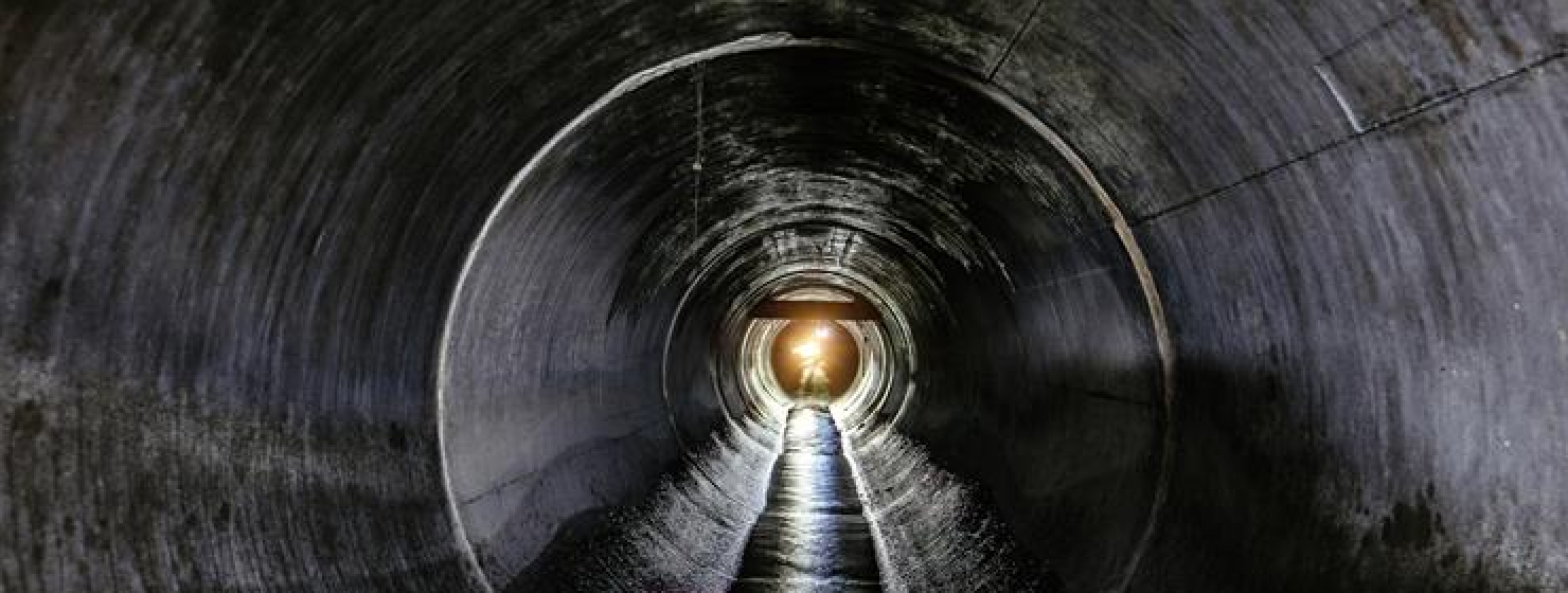 View looking through a long, concrete tunnel with light visible at the far end.