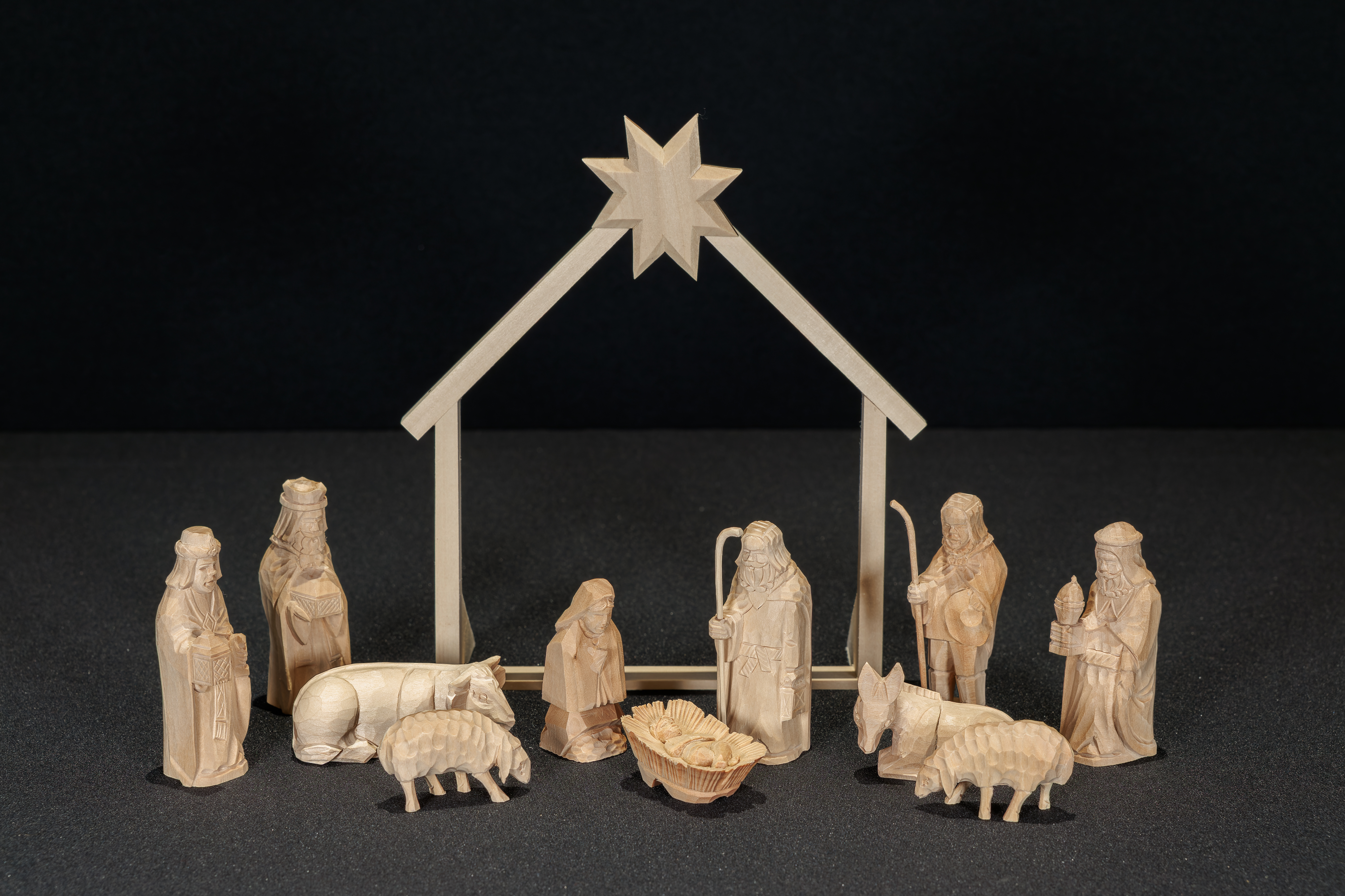 Wood carved Nativity with the Holy Family in front a stable frame. Flanking the stable are 3 Magi, a Shepherd, donkey, ox, and two sheep.