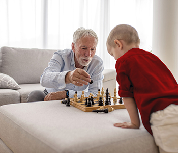 Starejši moški - verjetno sesek v dnevni sobi na kavču vnučka uči igrati šah.
