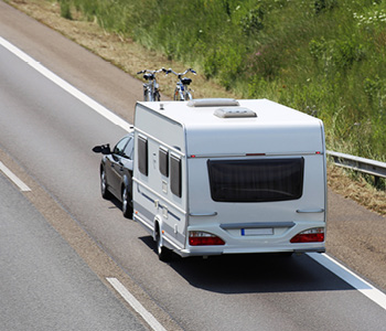 Vleka počitniške prikolice s črnim družinskim avtom na poletno kampiranje.