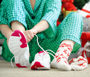 Trui prazniki so lahko zdravi - oseba v božičnih nogavicah in pižami obuva športne čevlje