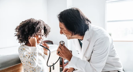 Male pediatrician kneeling down to young African American girl listening to stethoscope 
