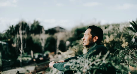 Asian man sitting on the ground outdoors with his eyes closed 