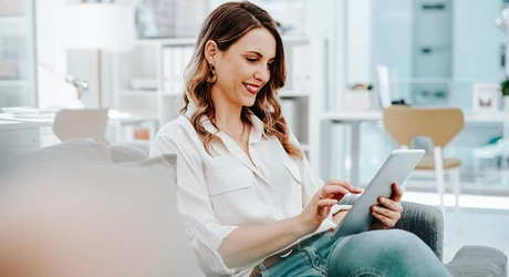 Woman seated on sofa in brightly lit office looking at tablet 