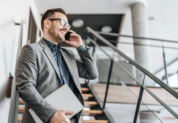 Smiling businessman talking on phone walking down staircase in open office 